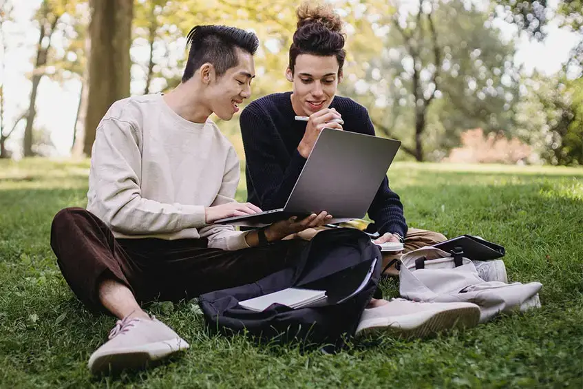 two guys computer coding job sitting on grass in a park